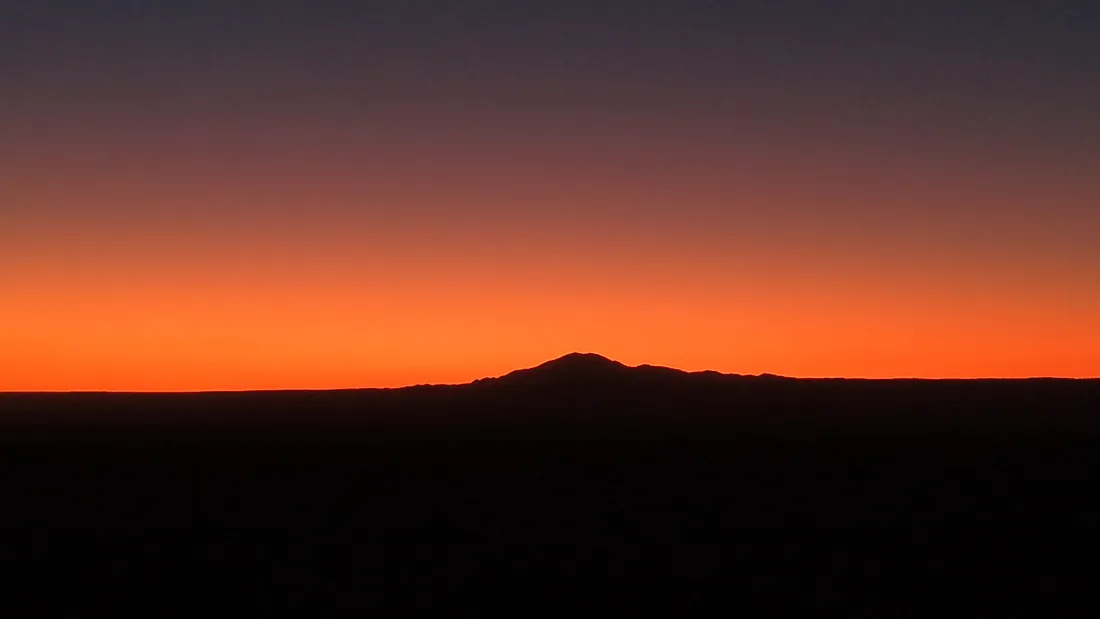Silhouette of Kimal hill against an orange dusk